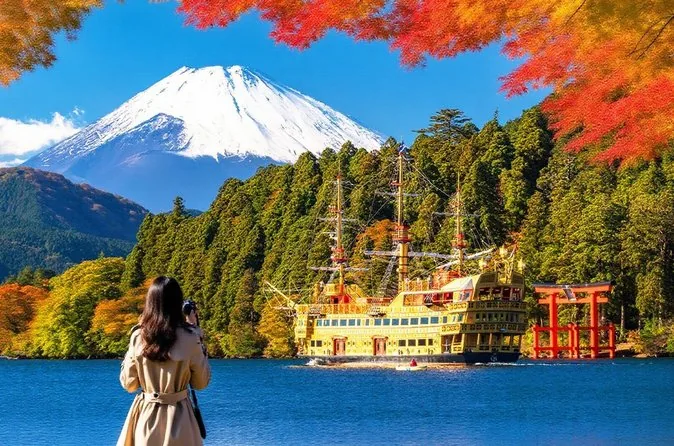 Une femme vue de dos regardant un bateau pirate sur un lac avec le Mt Fuji et des érables rouges